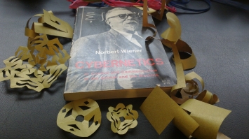 paper curlicues and other papercraft surrounding a copy of Norbert Wiener's Cybernetics